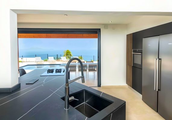 Réalisation Artego à Baie-Mahault cuisine noire avec plan de travail effet pierre et vue dégagée, conçue sur mesure pour un espace contemporain et ouvert.